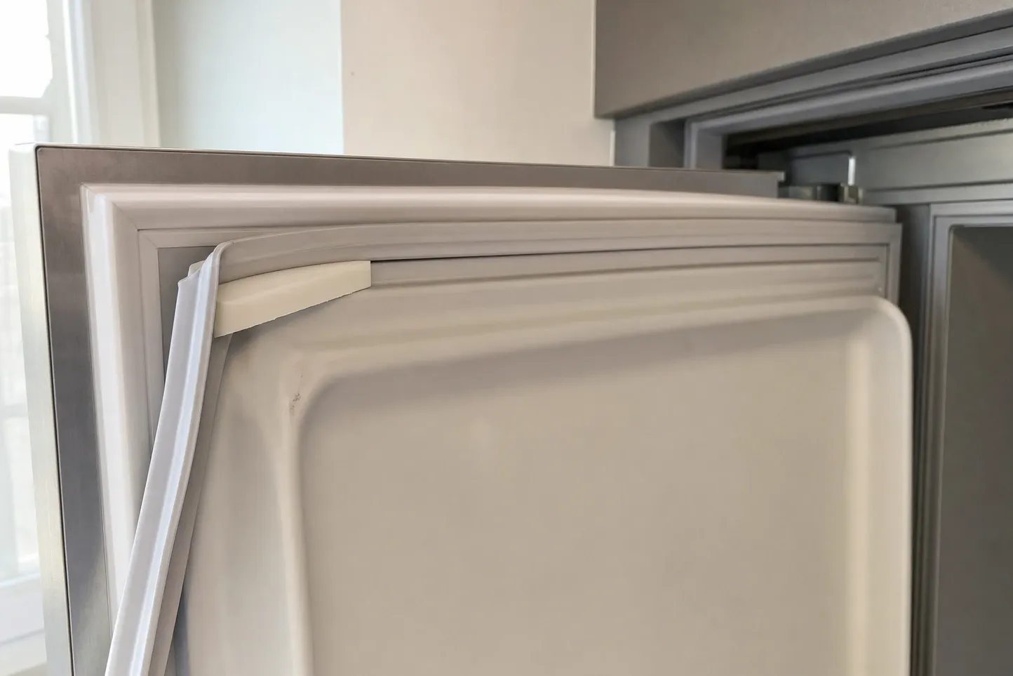 Close-up of a magnetic door gasket pulled loose along the top edge of a refrigerator door liner